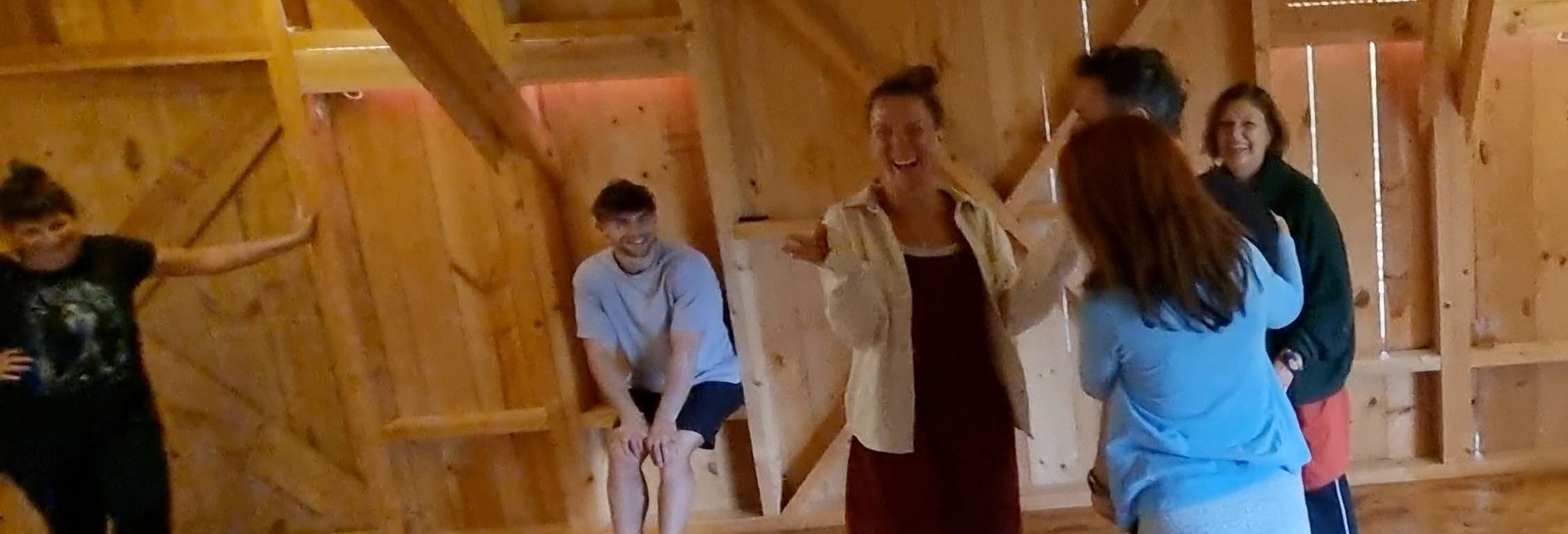 Un gruppo di partecipanti al corso ride insieme in una sala di legno chiaro: una donna al centro si porta una mano al viso mentre gli altri la guardano.